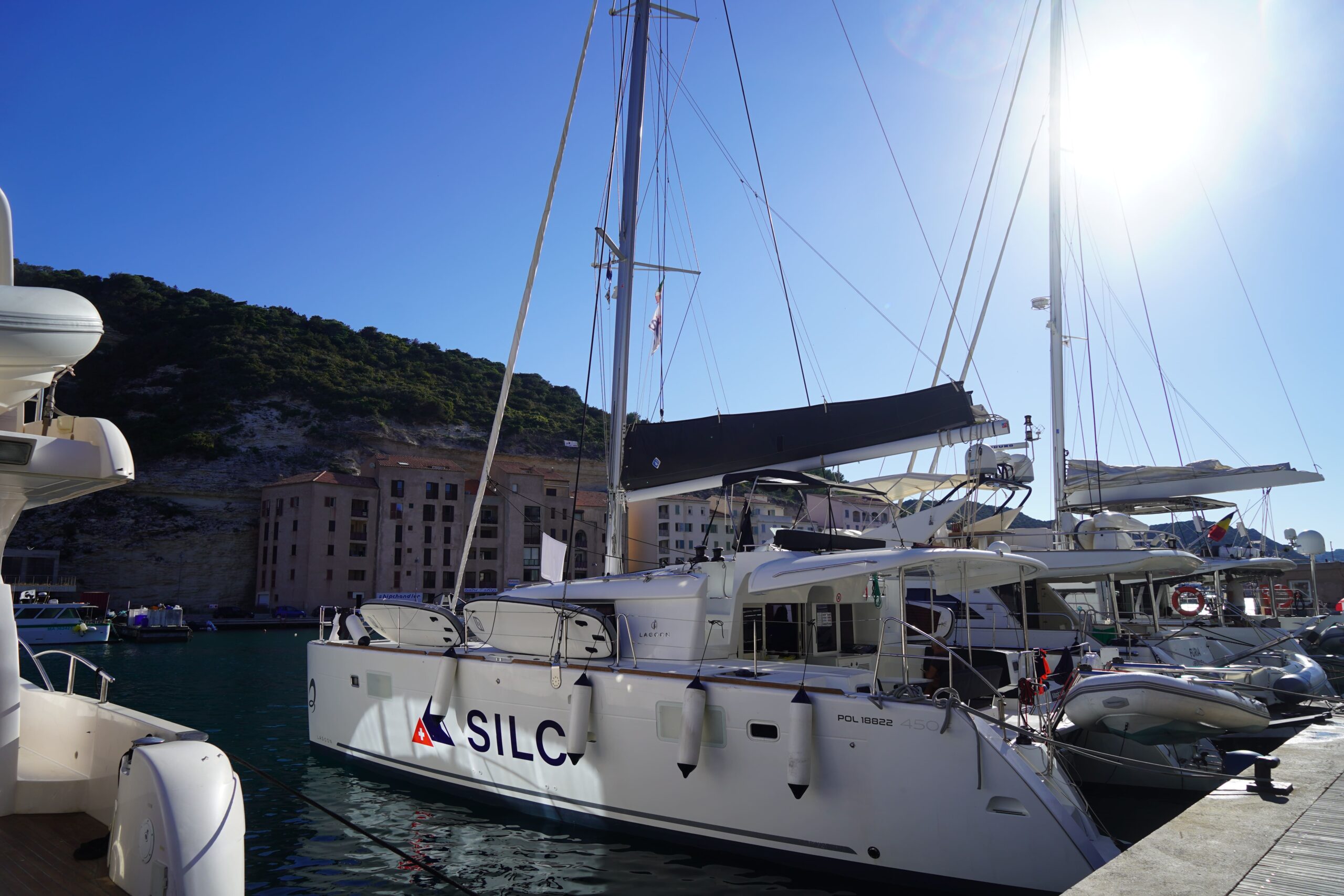 Sailing catamaran moored at a sunny marina with hillside and waterfront buildings