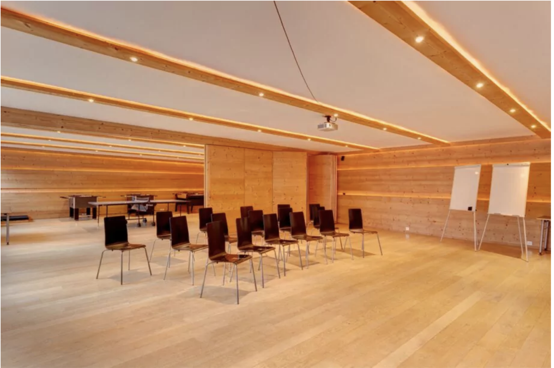 Modern wooden conference room with rows of chairs, projector, and flip charts under warm LED lighting