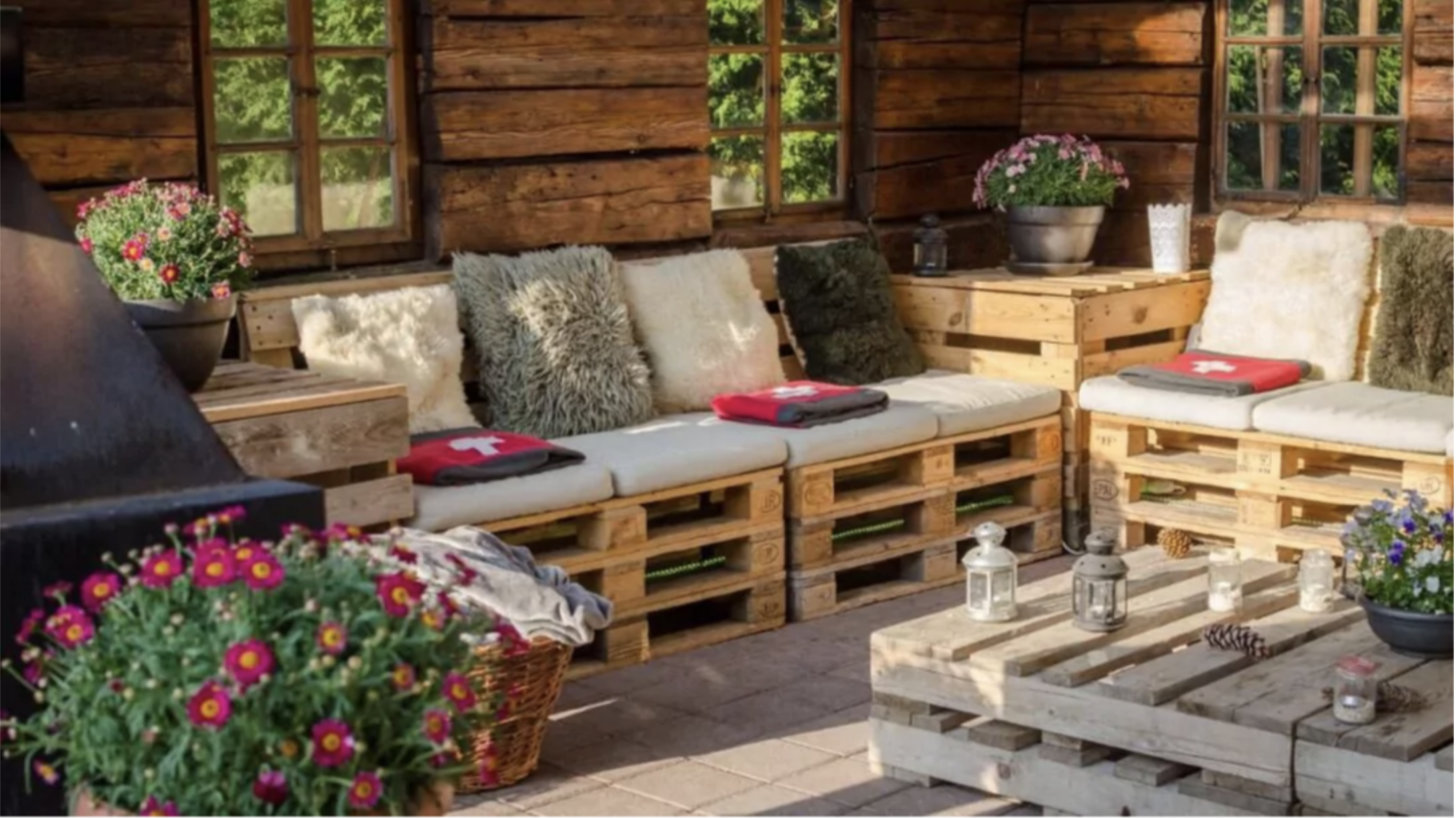 Rustic outdoor patio with pallet sofa and coffee table, cozy cushions, flowers, lanterns