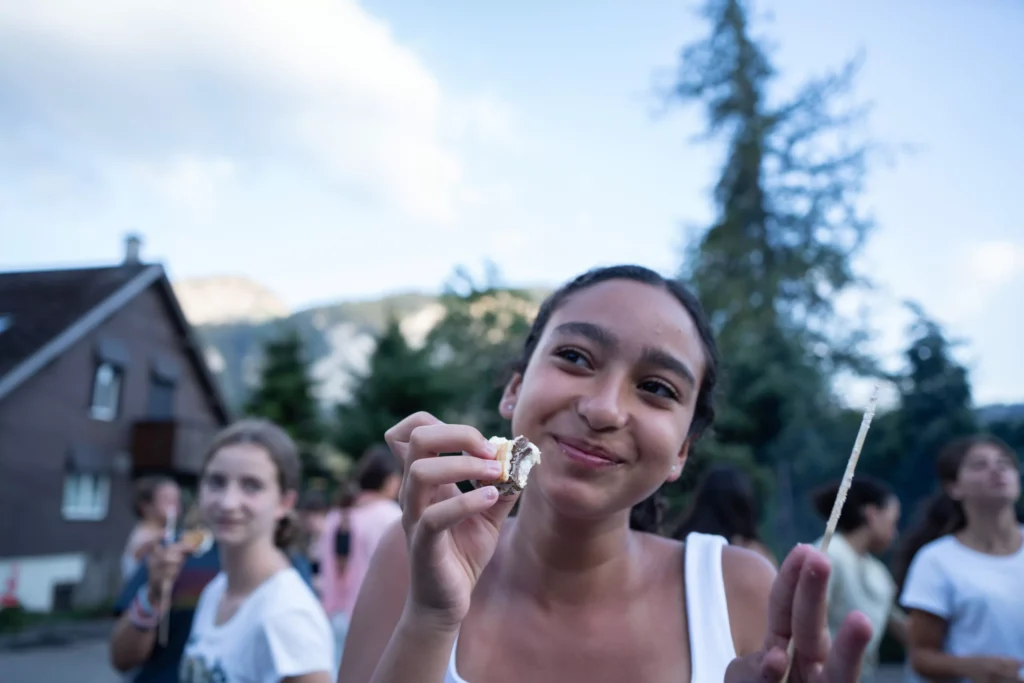 Smiling teen enjoys a s'more at an outdoor summer camp gathering