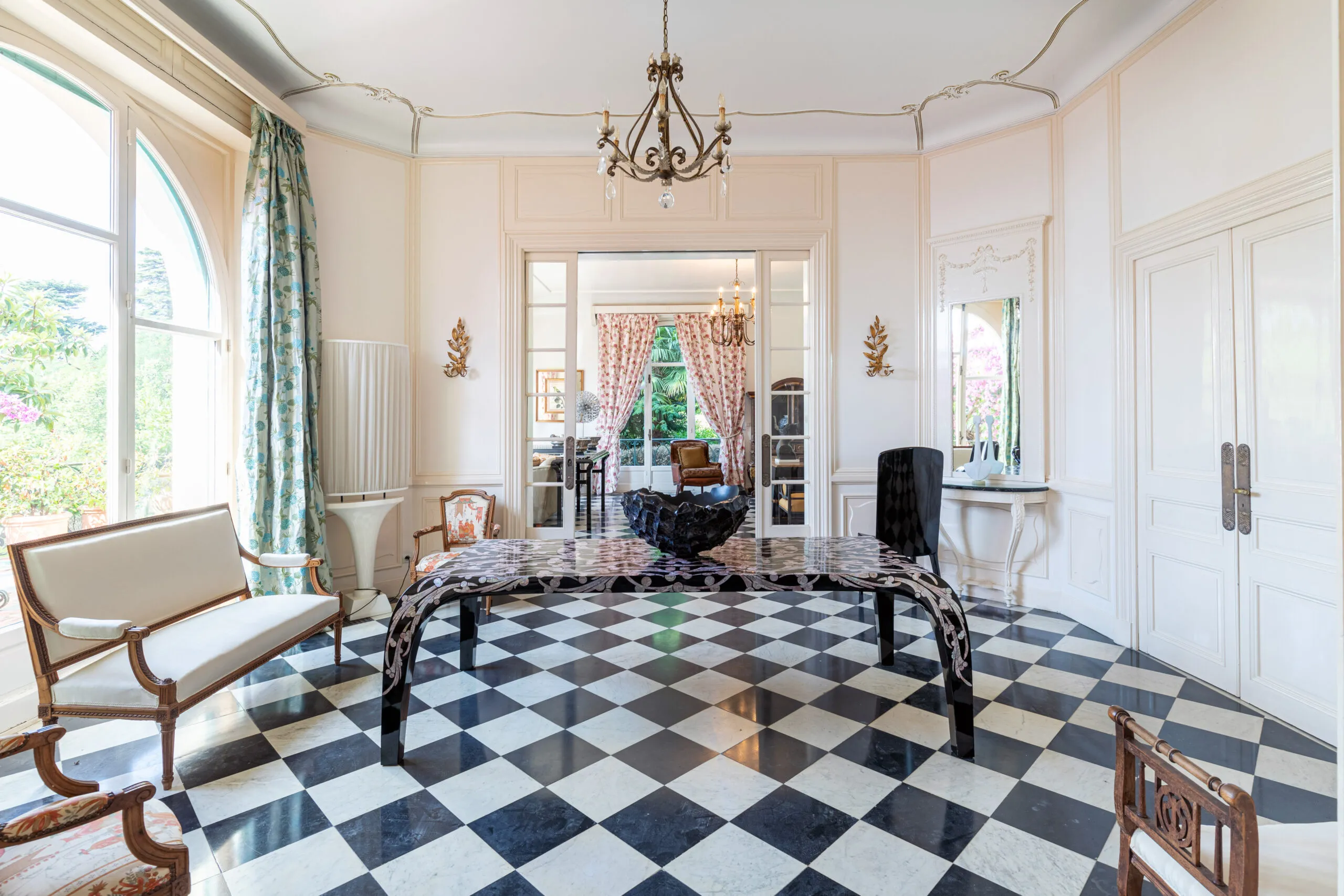 Luxury French salon with black-and-white checkerboard marble floor, ornate chandelier, and arched window