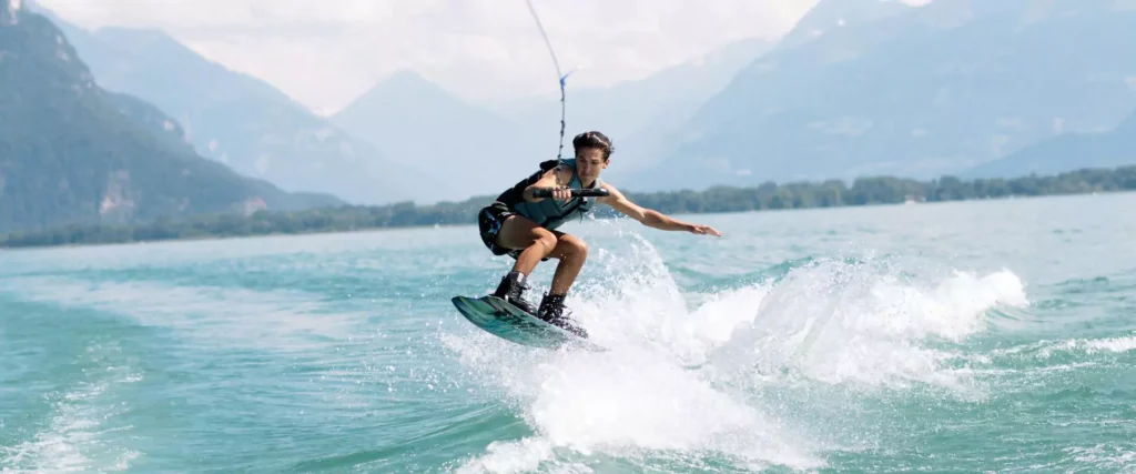 Wakeboarder catching air on a turquoise mountain lake with scenic peaks, action watersports.
