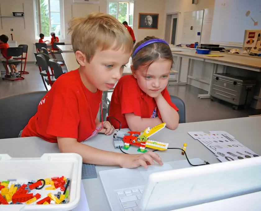 Children building a LEGO robotics kit and coding on a laptop in a STEM classroom