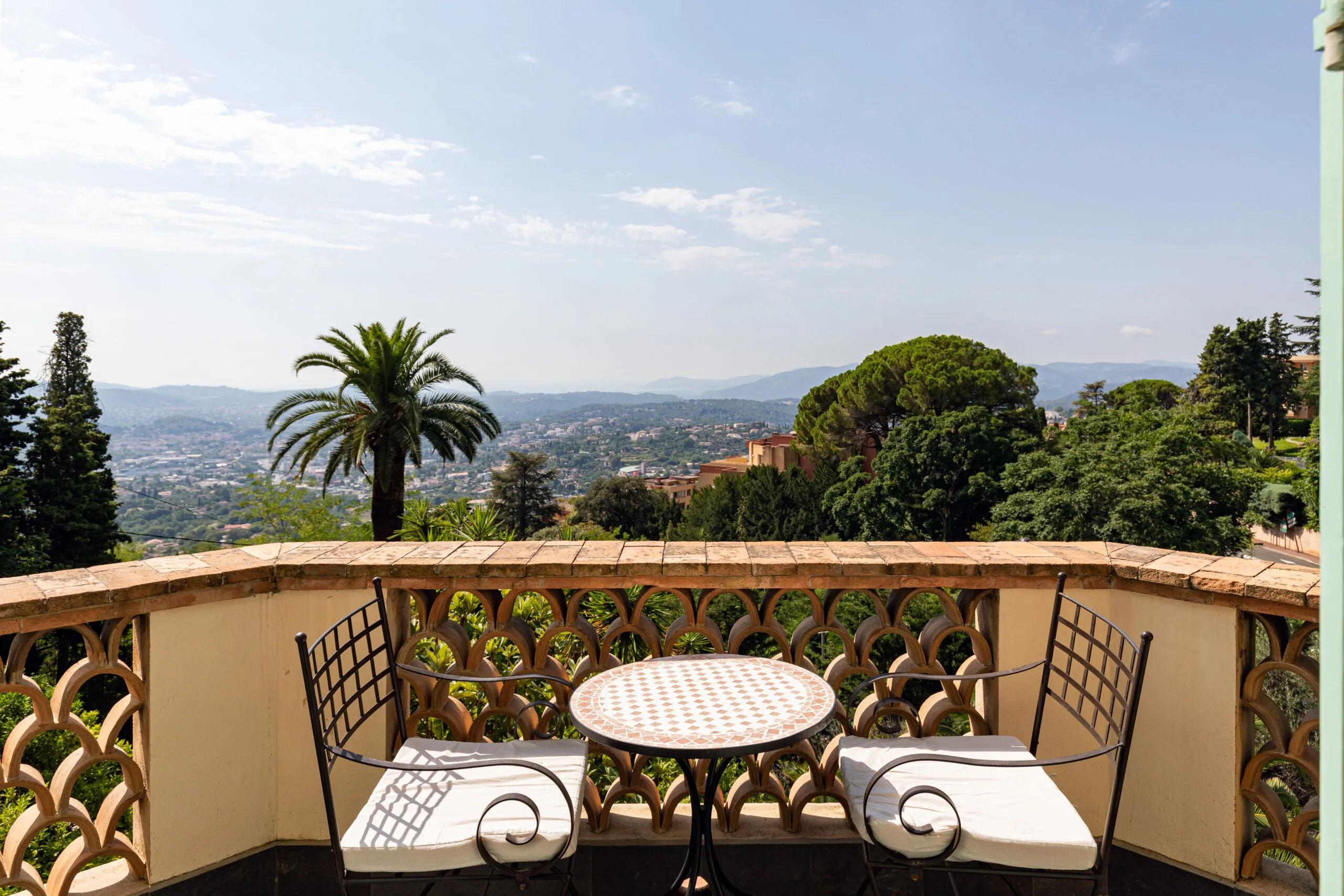 Mediterranean balcony with bistro table overlooking lush hills, cityscape and distant mountains for summer camp