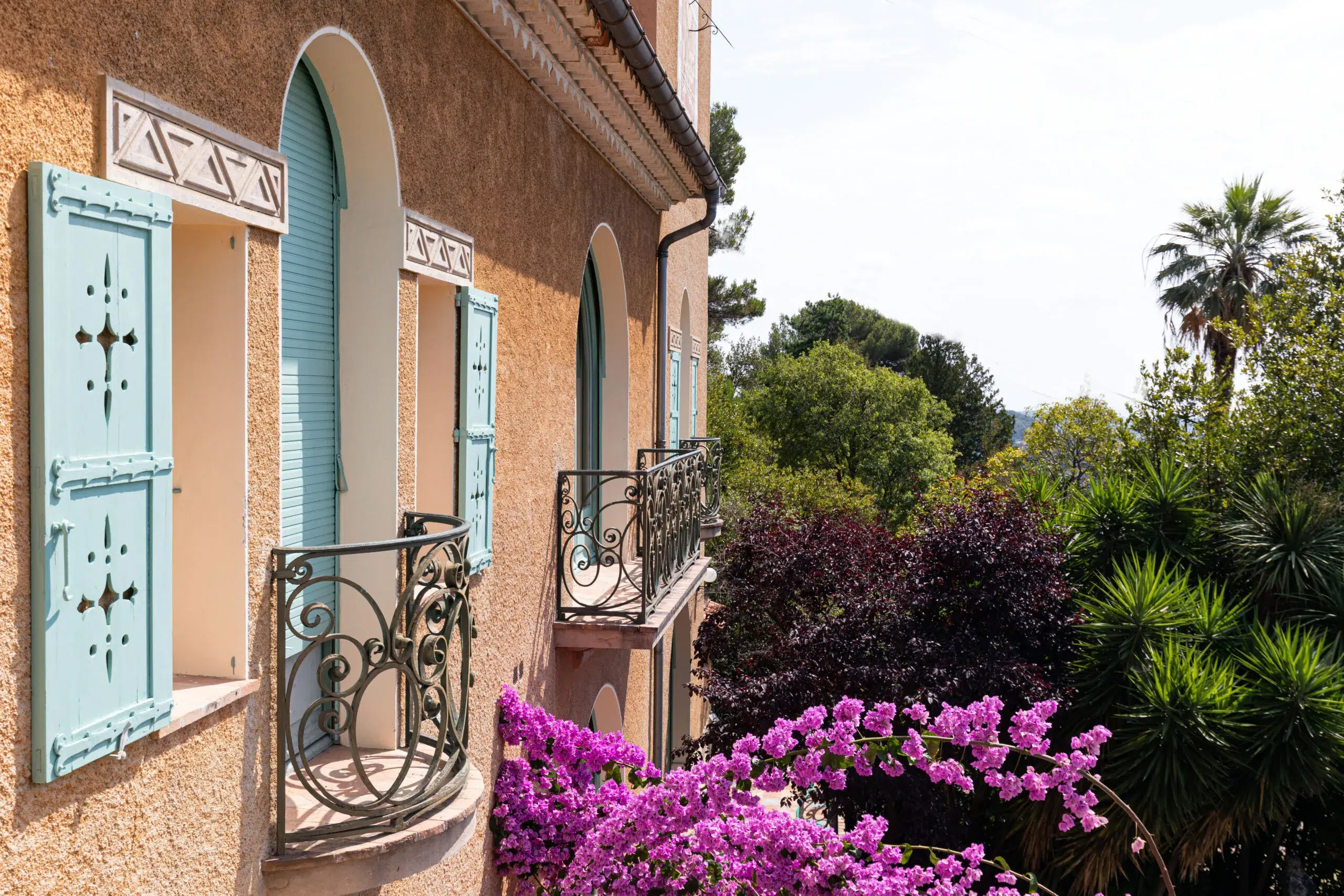 Mediterranean villa with mint shutters, wrought-iron balconies and bougainvillea overlooking lush garden