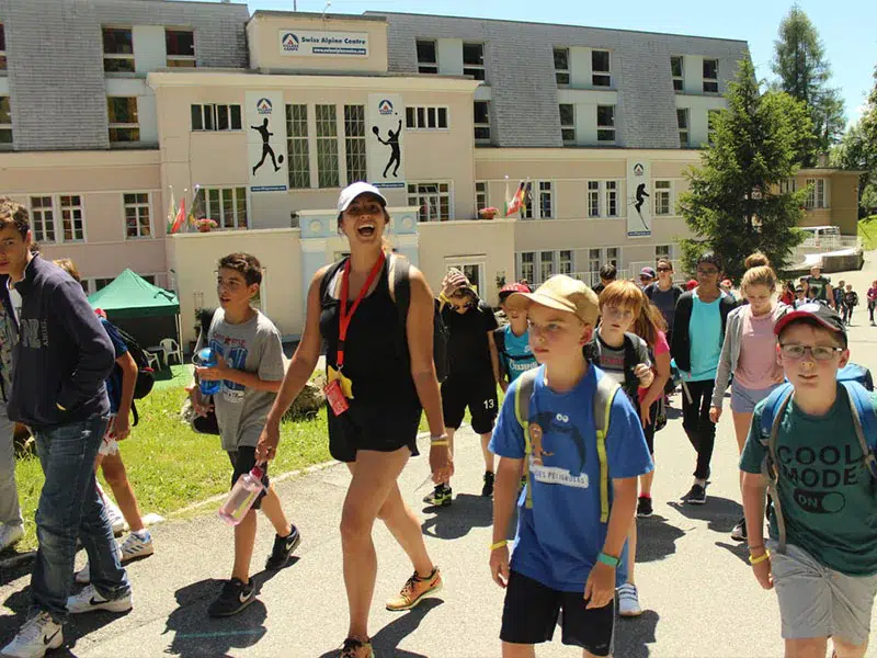 Group of children and camp counselor walking outside Swiss Alpine Centre during summer camp in Switzerland