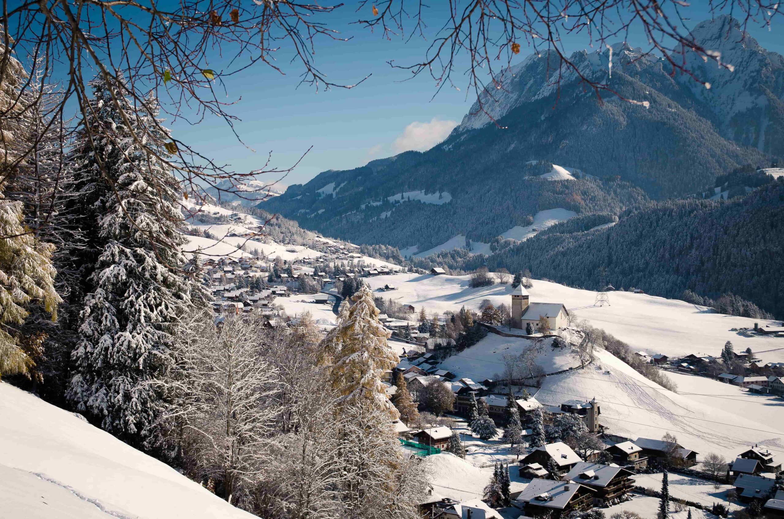 Snowy alpine village and church beneath forested mountains on a clear winter day