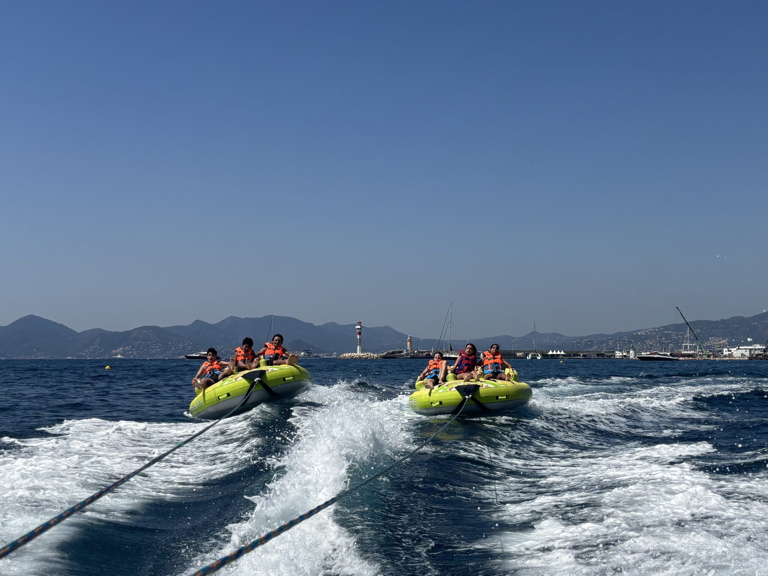 Water sports adventure: friends on towable tubes behind a speedboat near a coastal lighthouse