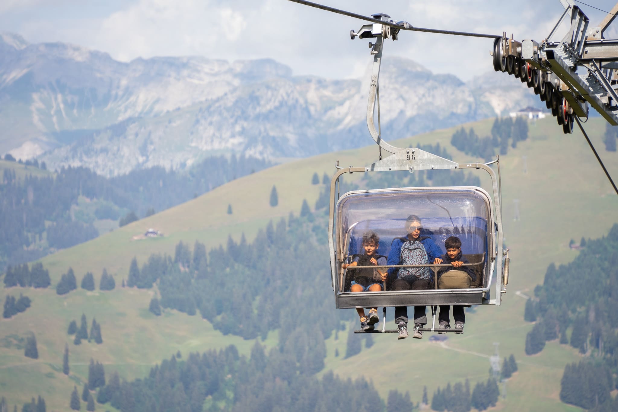 Family riding alpine chairlift with bubble canopy over scenic mountain landscape
