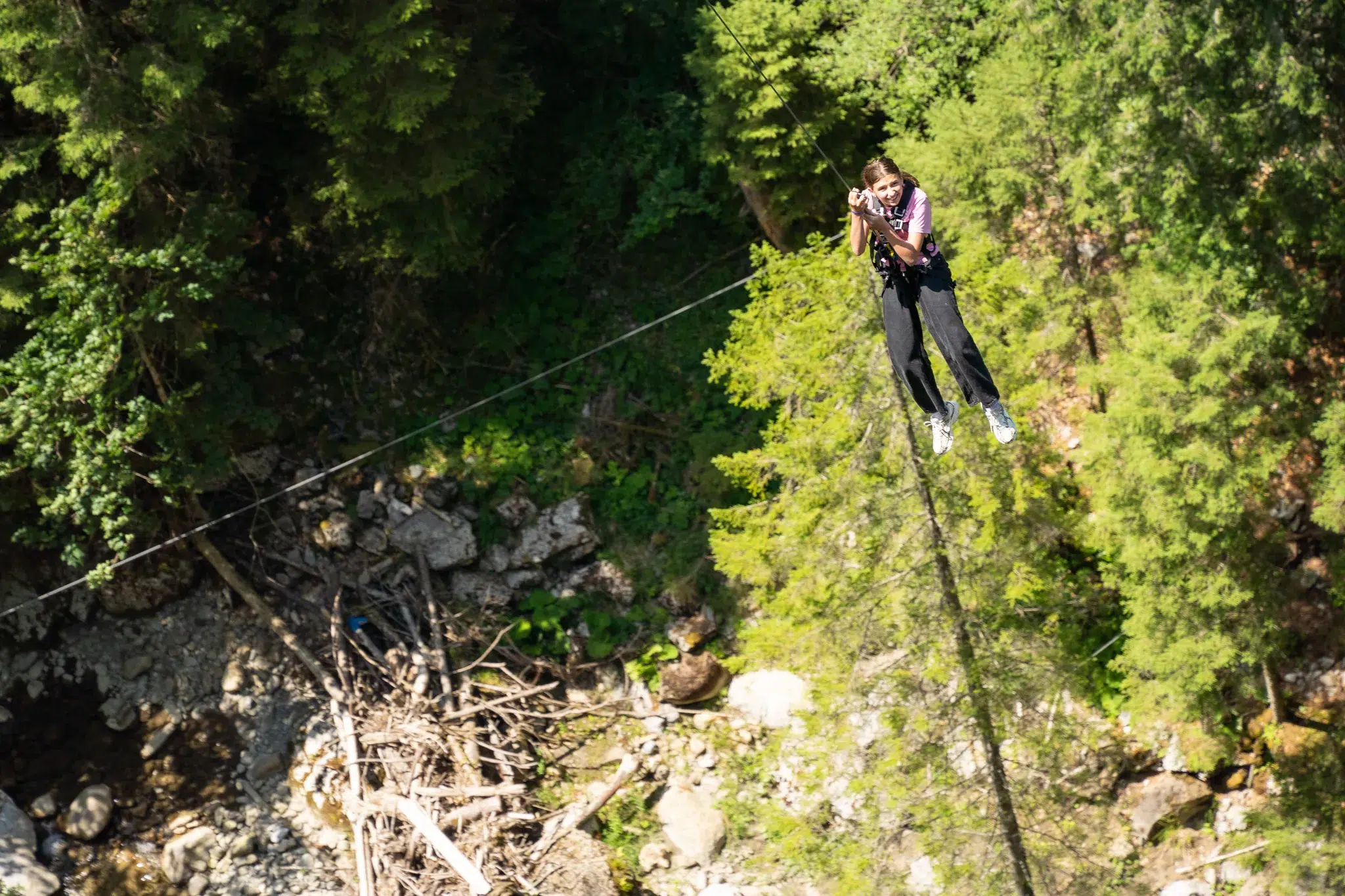Person ziplining high above a forested canyon, wearing a safety harness