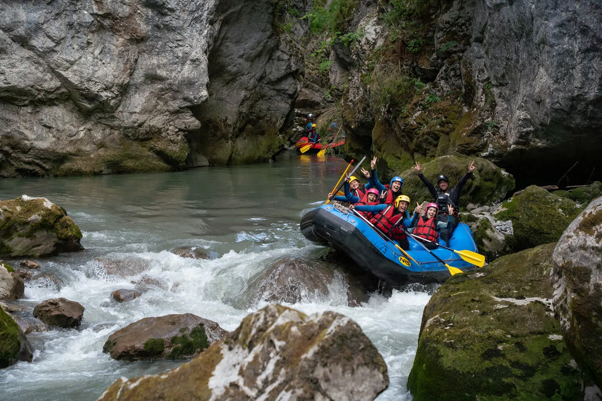 Guided whitewater rafting group navigating rapids in a rocky river canyon